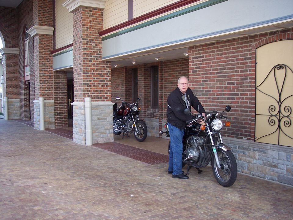 Two motorcycles parked outside a brick building, one with a man sitting on it