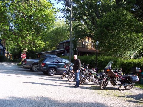 1985 Ford LTD Crown Victoria - Motorcycles and vehicles parked in a lot with trees and buildings in the background.