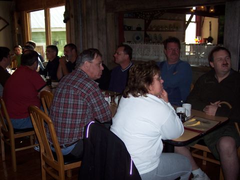 1985 Ford LTD Crown Victoria - A group of people are seated at tables in a restaurant, some looking towards the camera and others looking away.