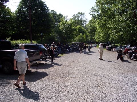 1985 Ford LTD Crown Victoria - A gravel parking lot is filled with motorcycles and cars, with several people standing around.