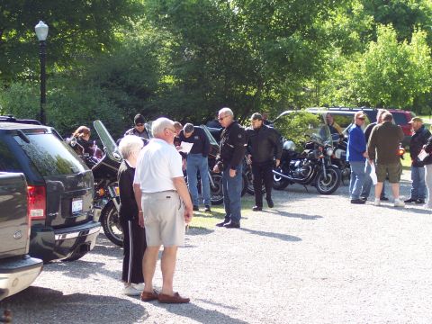 1985 Ford LTD Crown Victoria - People stand around motorcycles and SUVs in a parking area on a sunny day.