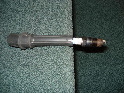 1999 Ford Crown Victoria - A spark plug with its black boot is shown against a textured background.