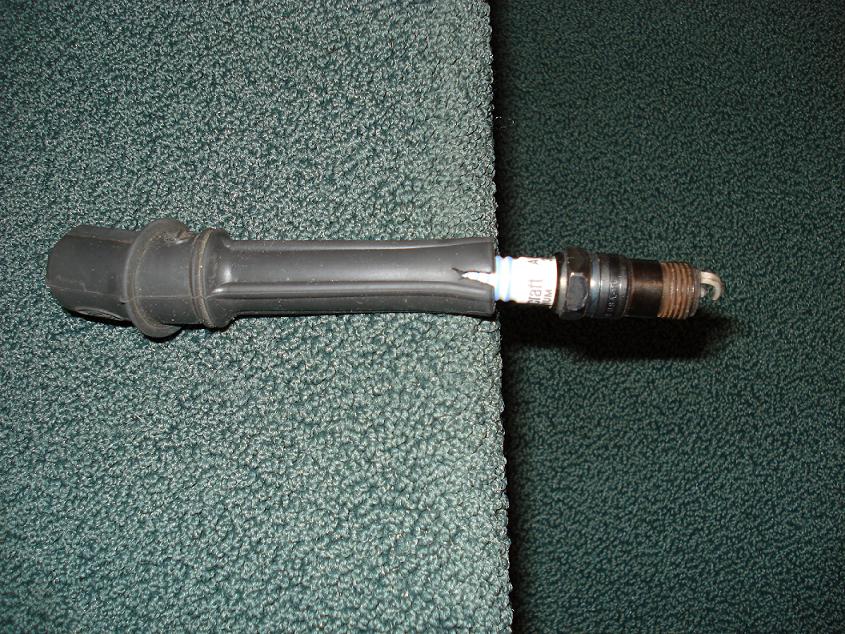 Black coil-on-plug boot with a used spark plug fitted, lying on green carpet