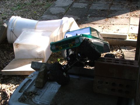 1996 Ford Bronco - An RC truck body is mounted on a chassis, resting on debris and bricks in an outdoor setting.