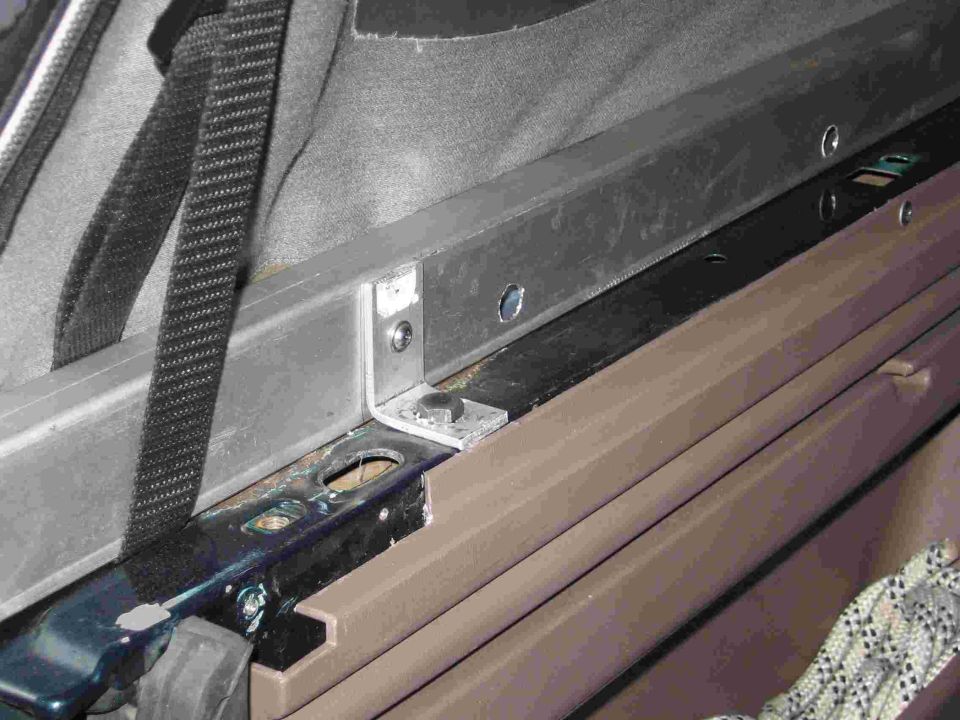 Aluminum L-bracket bolted to black soft-top rail above brown interior trim panel in a Bronco