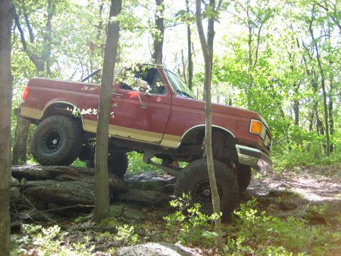 1990 Ford Bronco - This lifted 1990 Ford Bronco tackles a challenging off-road course amidst a wooded environment.