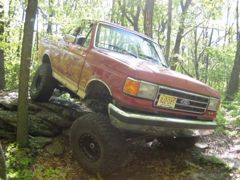 1990 Ford Bronco - This red SUV is navigating a rocky trail in a wooded area, its off-road capabilities.