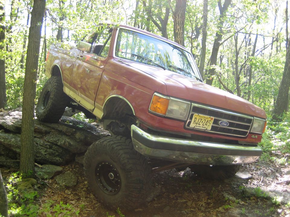 Red SUV with large tires on rocks in woods. License plate RJZ-245