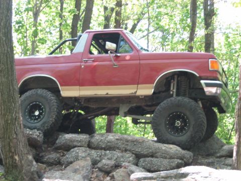 1990 Ford Bronco - 1990 Ford Bronco tackling rough terrain on a wooded trail.