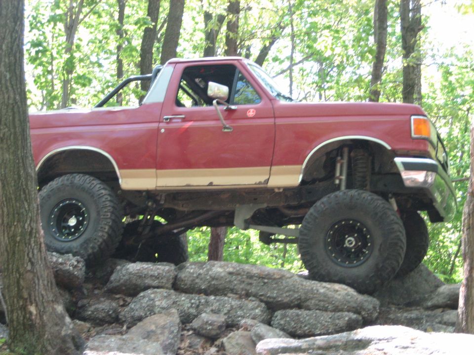 Red 1990 Ford Bronco with lifted suspension and large tires navigating a rocky trail