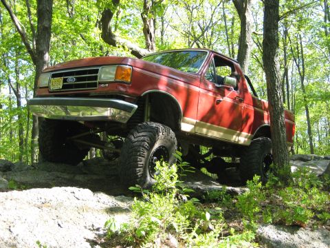 1990 Ford Bronco - This lifted 1990 Ford Bronco navigates a challenging rocky path through a wooded area.