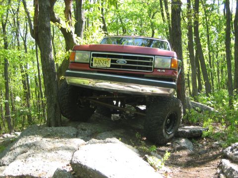 1990 Ford Bronco - Ford Bronco navigating a challenging rocky trail in a wooded area.