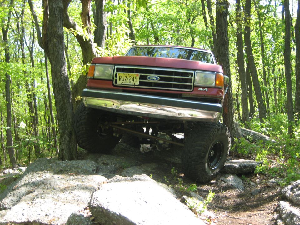 Red Ford Bronco with lifted suspension and large tires navigating rocky terrain