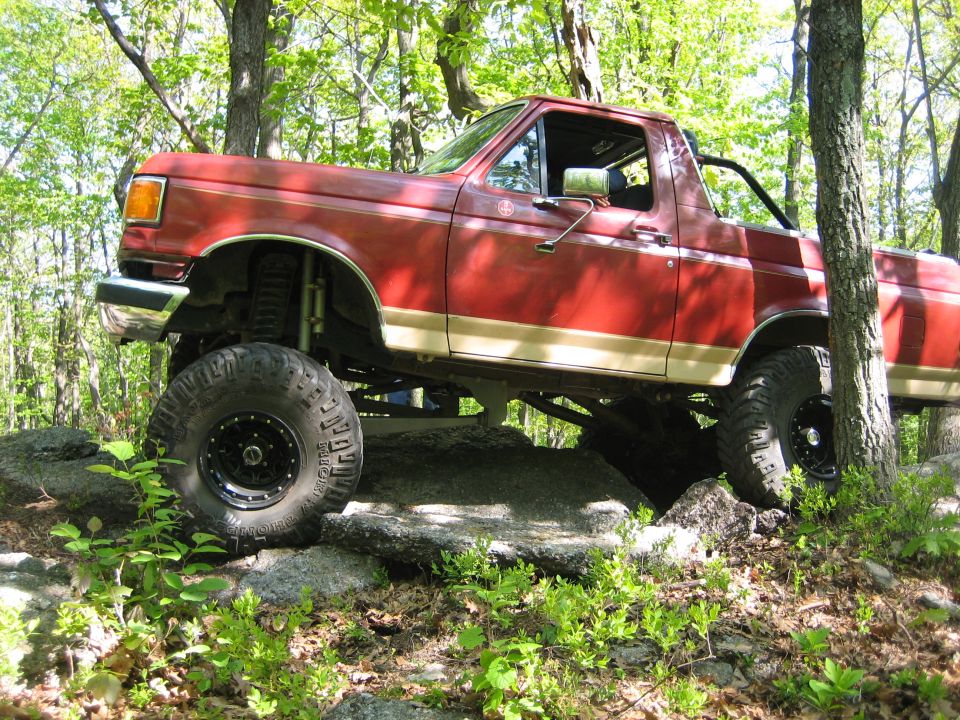Red lifted SUV with large tires navigating rocky terrain in a wooded area