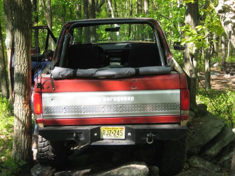 1990 Ford Bronco - This red Ford Bronco, likely from the late 1980s, navigates rocky terrain in a wooded area.