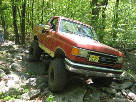 1990 Ford Bronco - Ford Bronco tackling a challenging off-road trail with large rocks.