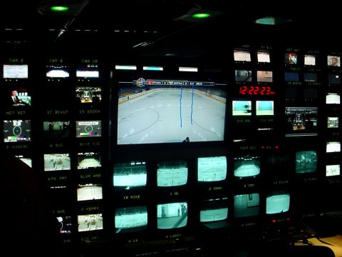 2000 Ford Taurus - A dark room filled with monitors displaying a hockey game and other video feeds, with a digital clock showing 12:22:23.