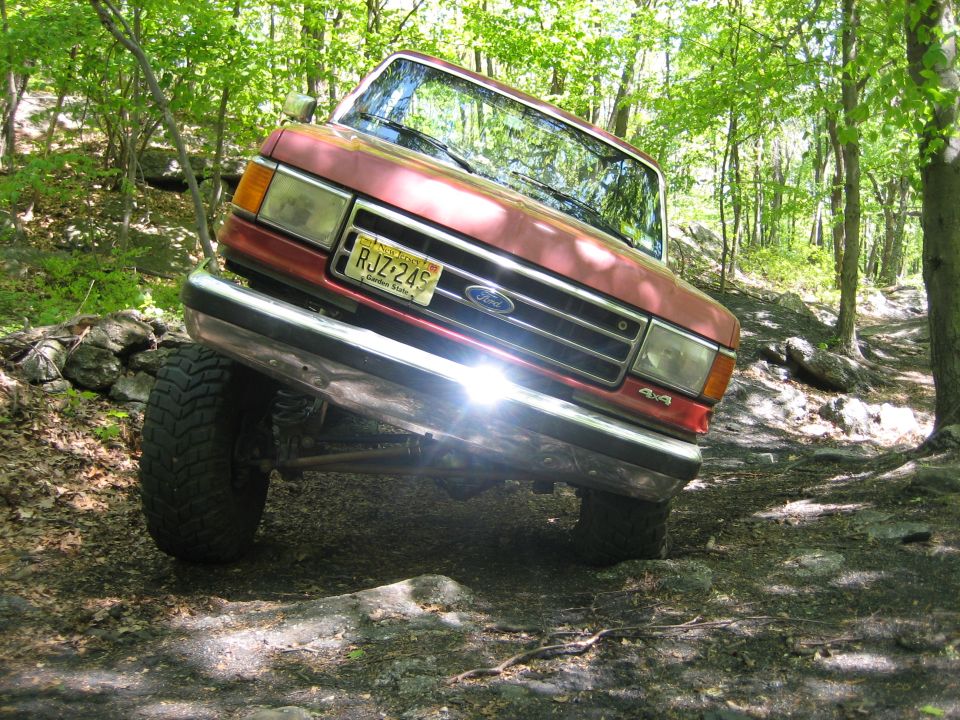 1990 Ford Bronco tilted on rocky trail, front grille and license plate visible