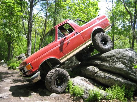 1990 Ford Bronco - Red 1990 Ford Bronco navigating a rocky off-road course.