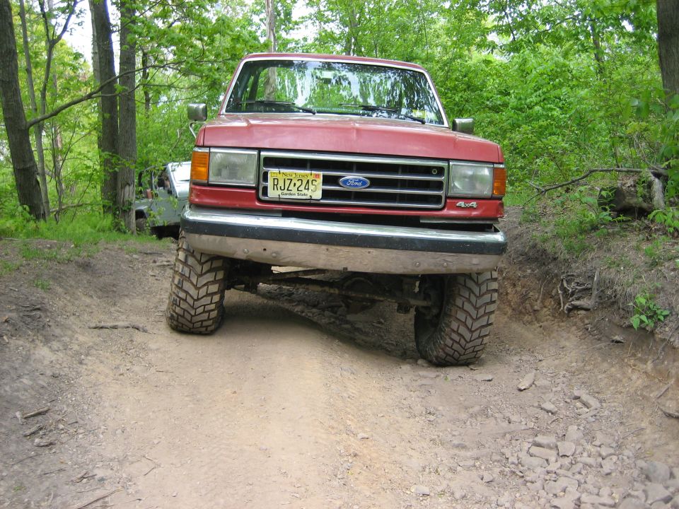 Red 1990 Ford Bronco front view on dirt trail with 4x4 badge