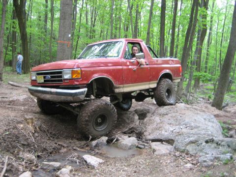 1990 Ford Bronco - This red Ford Bronco navigates a rocky trail in a forest setting.
