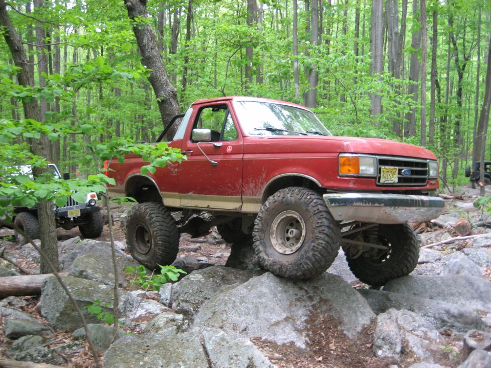 Red 1990 Ford Bronco on rocks, front 3/4 view