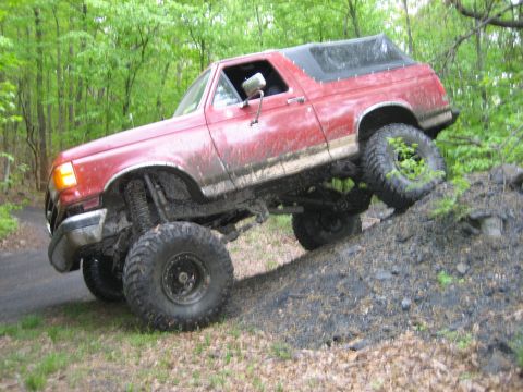 1990 Ford Bronco - This lifted Ford Bronco is navigating a steep, muddy incline during an off-road excursion.
