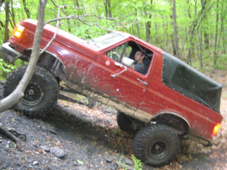Red 1990 Ford Bronco climbing a muddy incline