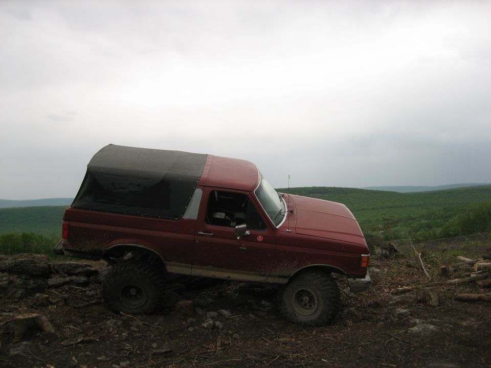 Red Ford Bronco with a black soft top, lifted with large tires, parked on a dirt hill