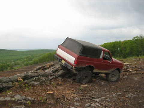 1990 Ford Bronco - A lifted red Ford Bronco navigates a challenging rocky incline off-road.