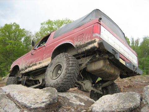 1990 Ford Bronco - Red 1990 Ford Bronco with a soft top is shown off-roading over rocks.