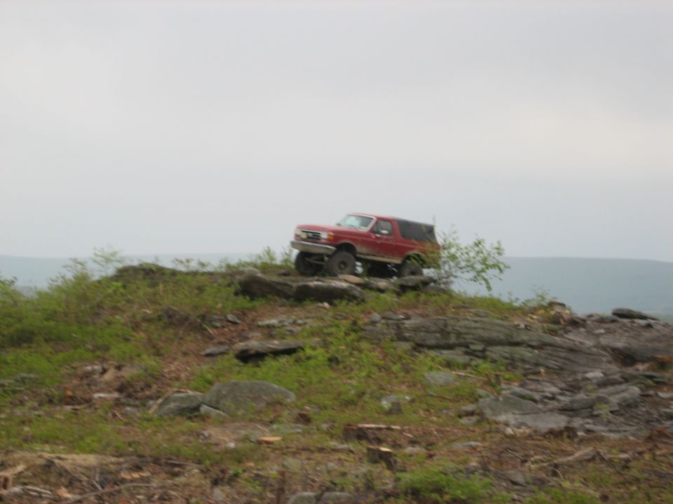 Red SUV on rocky terrain, front 3/4 view, lifted suspension, cloudy sky