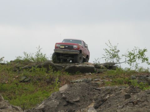 1990 Ford Bronco - A red 1990 Ford Bronco navigates a challenging rocky obstacle course.