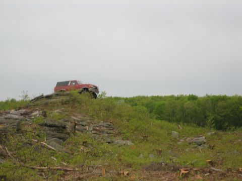 1990 Ford Bronco - A red SUV navigates a challenging, rocky incline under an overcast sky.