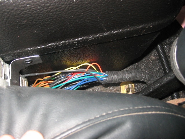 Close-up of a bundle of colorful wires, some exposed, under a vehicle's seat