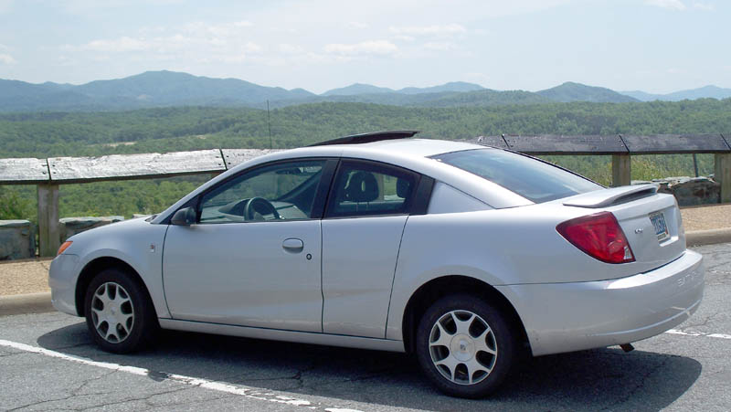 Silver coupe with a sunroof parked on asphalt with a mountain view