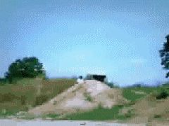 1987 Suzuki Samurai - An off-road vehicle is positioned on top of a dirt mound with trees and sky in the background.