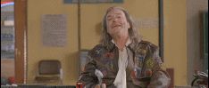 1987 Suzuki Samurai - A man with long hair and a patched jacket is seated indoors, with a poster visible on the wall behind him.