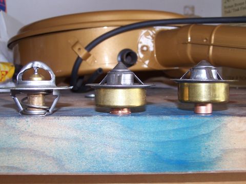 1973 Ford Ranchero - A close-up view of three automotive thermostats arranged on a surface, with a gold air cleaner visible behind them.