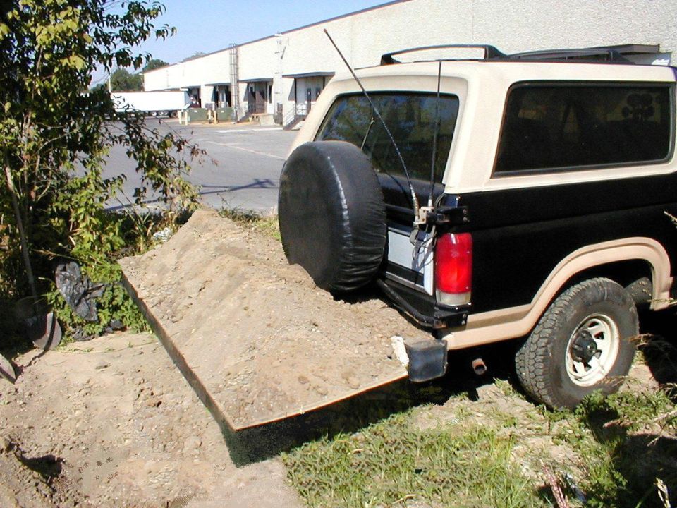 Two-tone Ford Bronco parked beside a dirt mound and metal ramp in an industrial lot