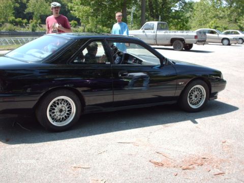1995 Ford Probe - A black coupe with a GT badge is parked in a lot, with two people standing behind it and other vehicles in the background.