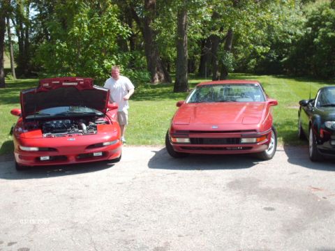 1995 Ford Probe - Two red Ford Probes are parked side-by-side in a grassy area with trees.