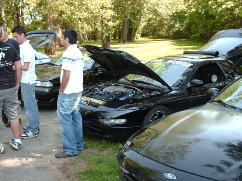 1995 Ford Probe - A group of people admire a black 1995 Ford Probe, with the engine exposed for viewing.