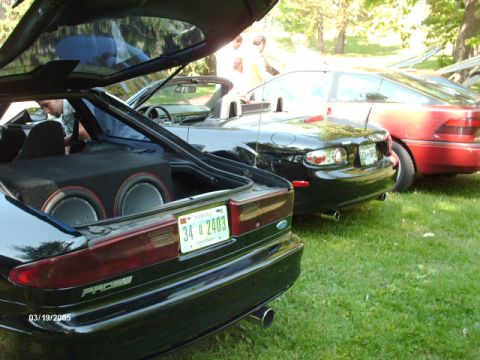 1995 Ford Probe - A black Ford Probe is parked on grass with its trunk open, revealing subwoofers.