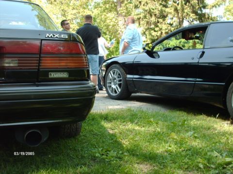 1995 Ford Probe - A black Ford Probe is parked next to a Mazda MX-6 Turbo, with people standing between them.