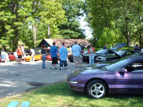1995 Ford Probe - A group of people gather around several cars, including a purple Ford Probe GT, on a sunny day.