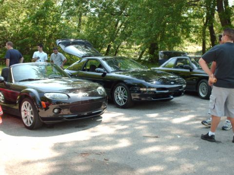 1995 Ford Probe - A trio of black sports cars are gathered outdoors, with one vehicle's rear hatch elevated.