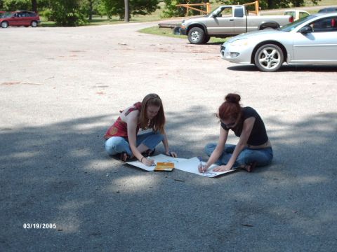 1995 Ford Probe - Two women draw on paper in a parking lot with several vehicles visible in the background.
