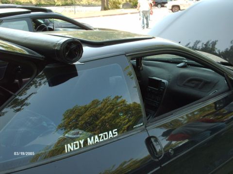 1995 Ford Probe - A black coupe is seen from the side, an aftermarket exhaust pipe mounted on the roof and an 'INDY MAZDAS' decal on the window.