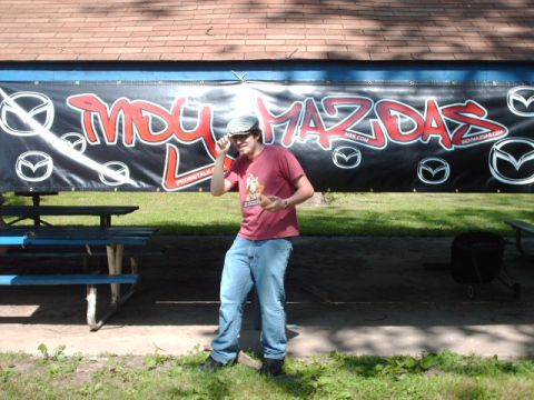 1995 Ford Probe - Man poses in front of a large banner for "INDY MAZDAS" at an outdoor event.